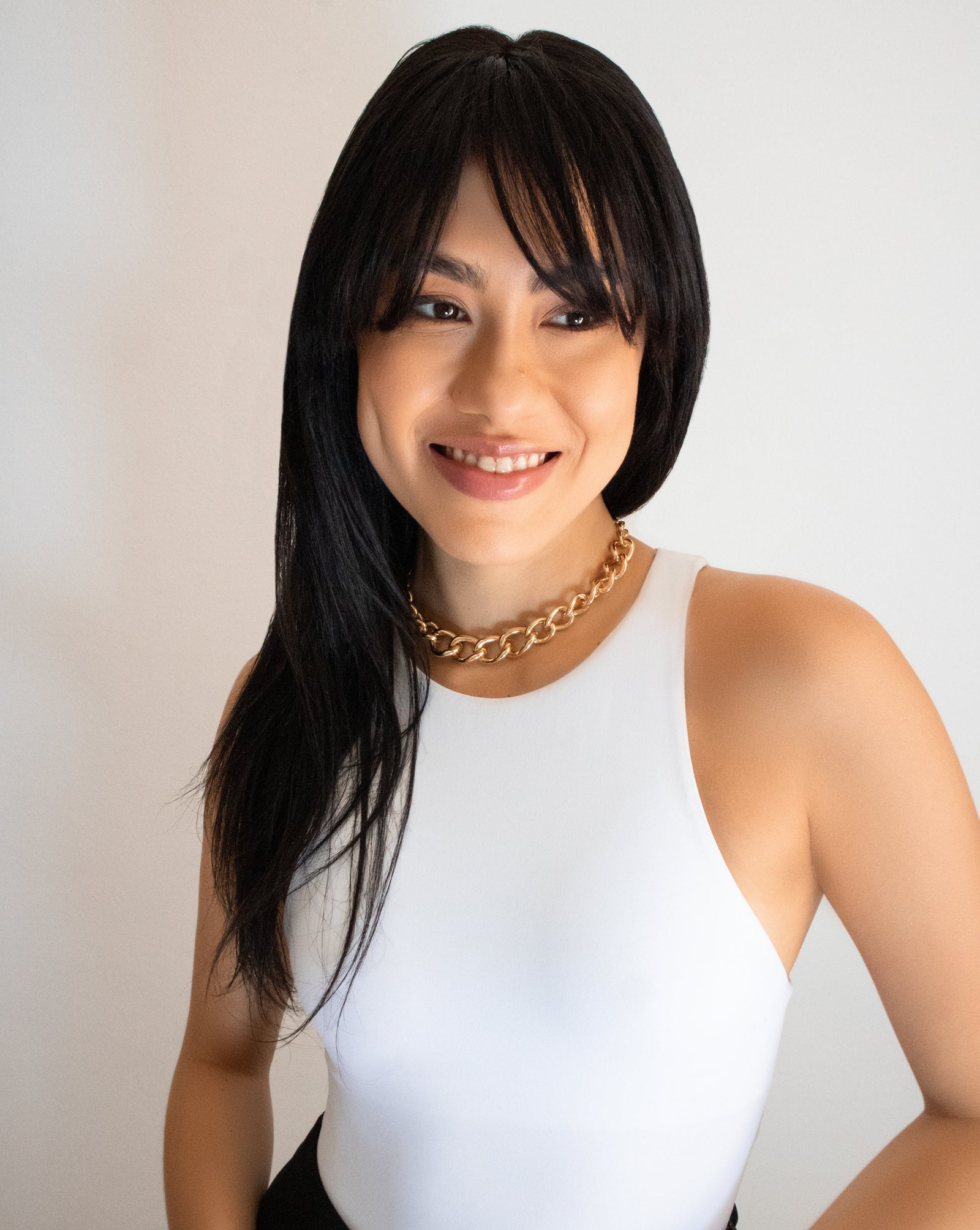 Stylish woman wearing long fringe wig wearing chunky gold chain necklace and white bodysuit