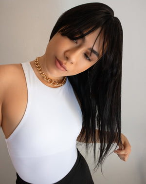 Stylish woman wearing long fringe wig wearing chunky gold chain necklace and white bodysuit
