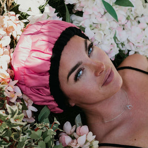 Woman wearing pink Lava Cap deep conditioning heat cap laying in field of flowers