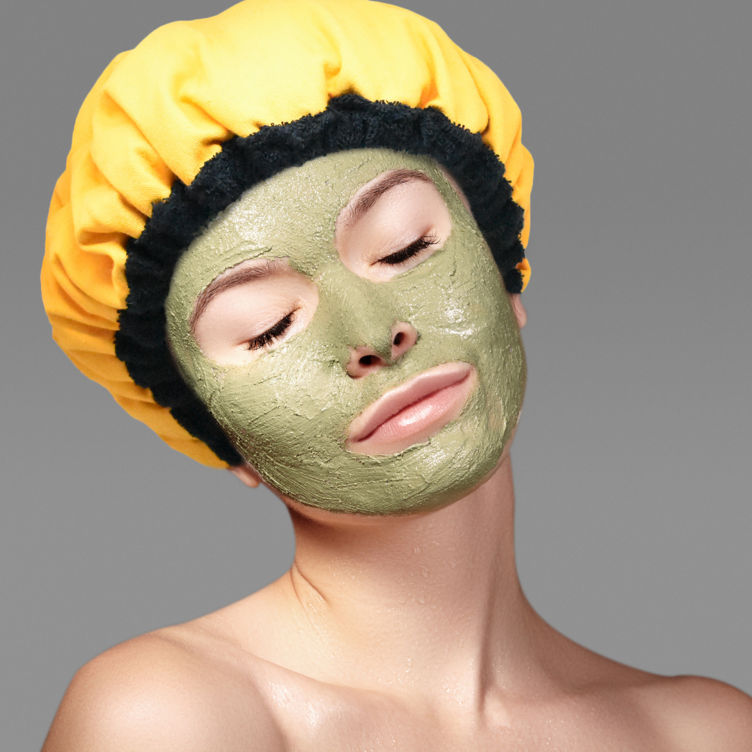 Woman wearing yellow microwavable flaxseed-filled deep conditioning heat cap while relaxing with clay face mask on